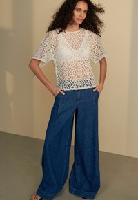Haut en dentelle avec un motif floral blanc et des manches courtes, associé à un pantalon en denim bleu à jambes larges. Texture lisse et coupe décontractée.