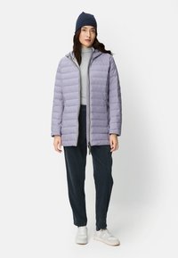 Hellviolette Steppjacke mit Kapuze, durchgehendem Reißverschluss, Seitentaschen und glatter Oberfläche, kombiniert mit dunkler Hose und weißen Turnschuhen.