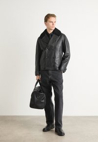 Musta nahkainen kaksirivinen takki, jossa on kauluksellinen kaulus, yhdistetty mustiin farkkuihin ja mustaan laukkuun. Rakennepinnat, minimalistinen muotoilu.