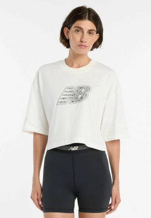 Kvinde iført en hvid kort crop-top med et blomstret "NB"-logo og sorte træningsshorts med høj talje med et "NB"-logo på taljebåndet.