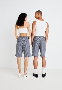 Stripete shorts i marineblått og hvitt, med lengde til midten av låret, baklommer og et tettsittende liv; kombinert med minimalistiske topper og fottøy.