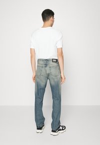 Jeans de denim azul claro con un lavado desgastado, diseño de pierna recta, cinco bolsillos y una etiqueta negra en la parte trasera. Combinados con una camiseta blanca.