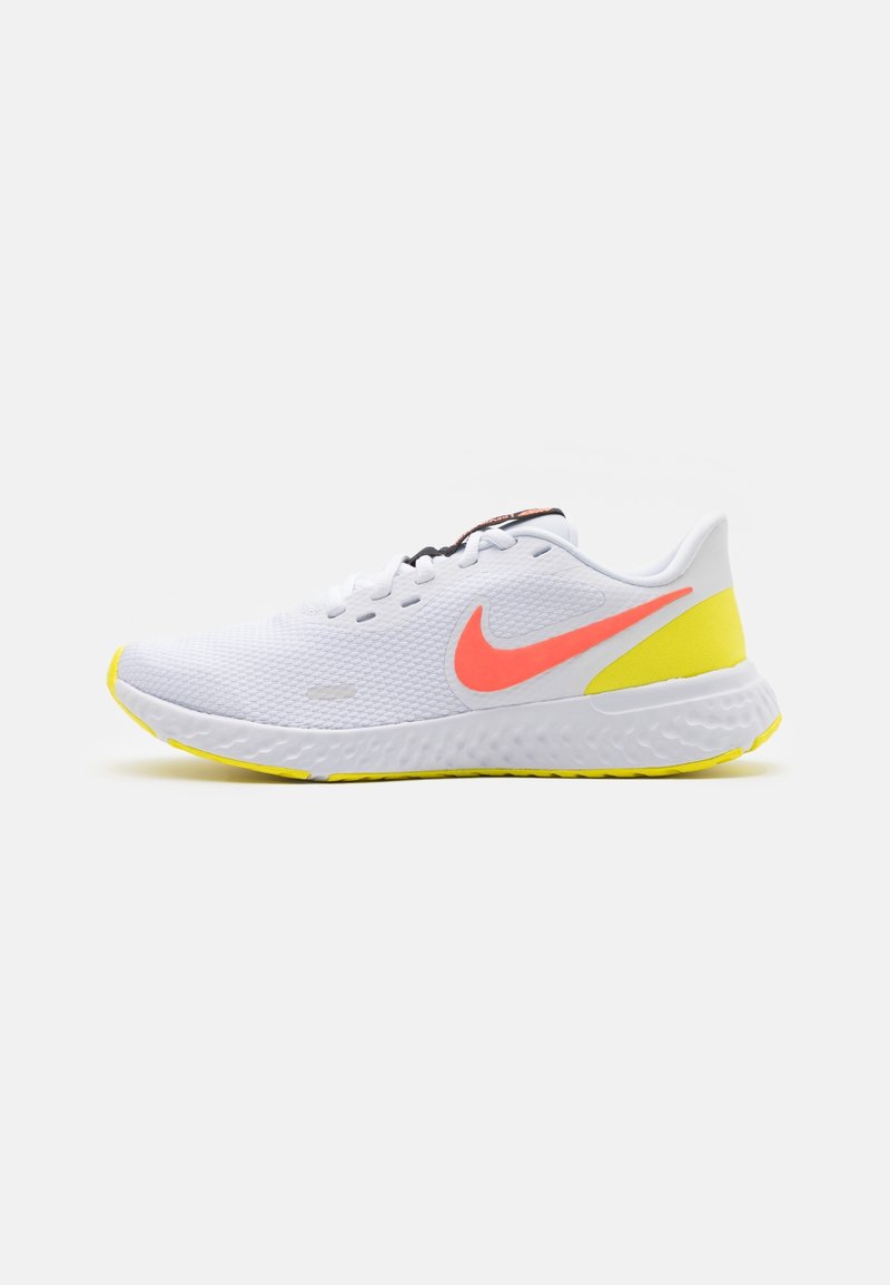 Bílé sportovní boty s prodyšným svrškem, růžový Nike swoosh, žluté akcenty na podrážce a texturovaný vzor. Obsahují černé šňůrky a polstrovanou podrážku.