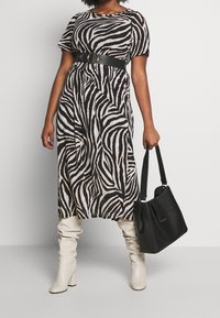 Sukienka midi w zebra print, z krótkimi rękawami, czarnym paskiem z okrągłą klamrą, zestawiona z wysokimi kremowymi kozakami i czarną torebką.