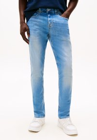 Jasnoniebieskie dżinsy o dopasowanym kroju, z pięcioma kieszeniami, subtelnymi przetarciami i jasnymi detalami szwów, zestawione z białymi trampkami.