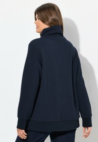 Mörkblå, texturerad fleece-pullover med hög krage. Har långa ärmar och en avslappnad passform, med ribbade ärmslut och nederkant.