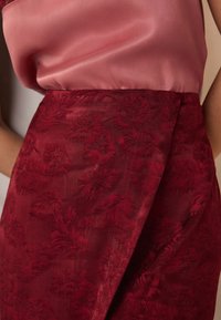 Piros virágmintás szövet texturált felülettel, sima rózsaszín szatén felsőrésszel párosítva. A ruhadarab átkötős derékrésszel rendelkezik.