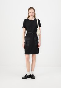 Black short-sleeve dress with a belt, featuring dual front pockets and a smooth texture. Paired with black shoes and white ankle socks.