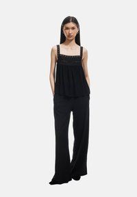 Top nero senza maniche con bordi in pizzo e pantaloni neri a palazzo. Entrambi i capi presentano una trama morbida e fluente e un design minimalista.