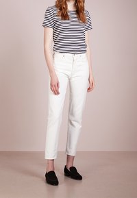 Randig t-shirt i marinblå och vit, vita raka jeans och svarta loafers. Slät bomullstyg, figurnära design och ankellång nederdel.