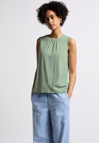 Sleeveless top in muted green, lightweight fabric, featuring a gathered neckline and a relaxed fit, paired with light denim wide-leg pants.