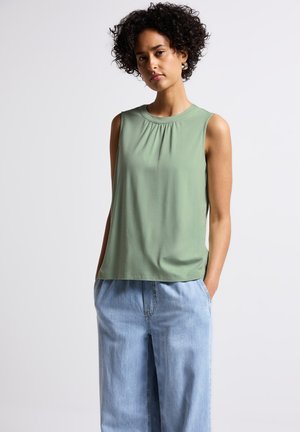 Top sin mangas en un verde apagado, de tela ligera, con un escote fruncido y un corte relajado, combinado con pantalones de mezclilla anchos de tela clara.