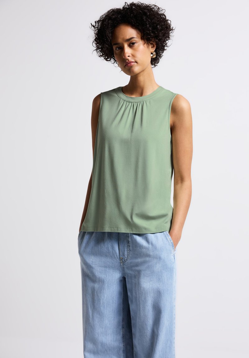 Sleeveless top in muted green, lightweight fabric, featuring a gathered neckline and a relaxed fit, paired with light denim wide-leg pants.