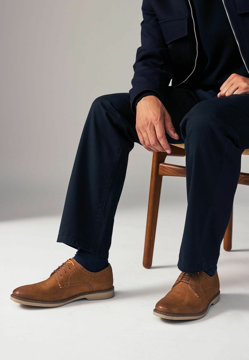 Zapatos de vestir de cuero marrón con un acabado suave, puntera redonda y diseño con cordones. Presentan costuras en contraste y una suela de goma ligera.