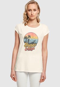 Cremefarvet bomulds t-shirt med et cirkulært grafik, der har palmetræer, en solnedgangsgradient og teksten "Stranger Things" i livlige farver.