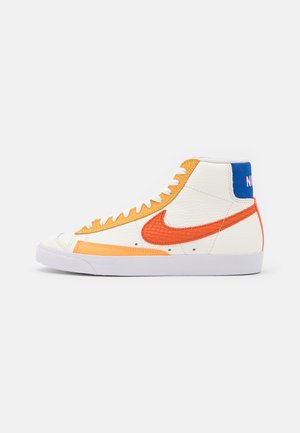 Højtop hvid sneaker med orange og gule accenter, blå hælflig, orange Nike swoosh og hvide snørebånd på hvid baggrund.