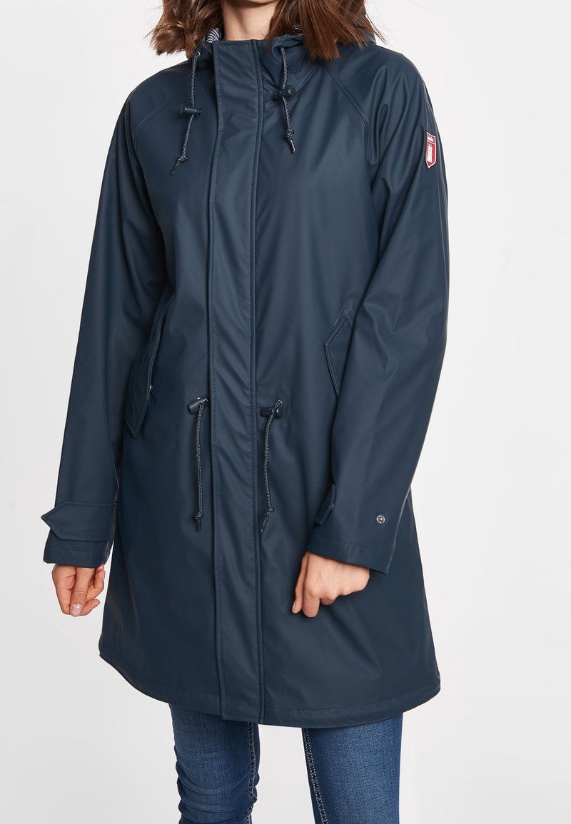 Marineblauwe waterdichte parka met trekkoordcapuchon, zijzakken en verstelbare manchetten. Glad textuur en lengte tot halverwege de dijen, met een subtiele logo.
