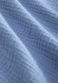 Hellblauer, strukturierter Stoff mit einem zerknitterten Muster. Weiches Material mit einem leicht durchsichtigen Erscheinungsbild und subtilen Farbvariationen.