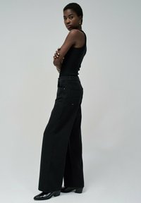Pantalones de mezclilla de pierna ancha negros, con una cintura alta, dos bolsillos traseros y combinados con zapatos de tacón negros. Diseño simple y limpio.