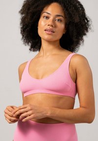 Rosa bralette i mjukt material, med breda axelremmar och låg halsringning. Slät textur med minimala sömmar och en figursydd design.