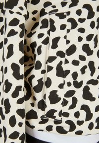 Tkanina s leopard printom u crno-bijeloj boji s teksturiranom površinom, koja sadrži vidljivu džep, a završena je s crnim rebrastim pojasom.