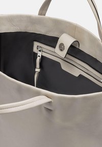 Hellgraue Leder-Tote mit schwarzem Innenfutter, ausgestattet mit einer Reißverschlusstasche und einem Druckknopfverschluss. Glatte Textur und robuste Griffe.