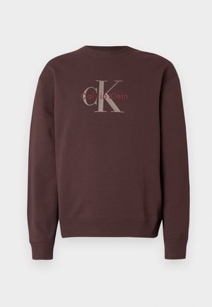 Brun sweatshirt med rund halsringning. Har "Calvin Klein"-logotyp i grått och vinrött på baksidan. Mjukt tyg med ribbade muddar och fåll.