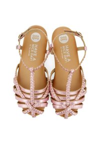 Sandalias de cuero rosa con tiras trenzadas y hebilla en el tobillo. Suela plana con planta texturizada, que presenta un logotipo impreso y texto.