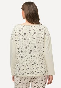 Lichtgekleurde sweatshirt met een sterrenpatroon in grijstinten. Zachte textuur, lange mouwen en een relaxte pasvorm. Bijpassende geklede broek is zichtbaar.