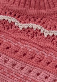 Vêtement en tricot de différentes nuances de rose avec des motifs ajourés et une accentuation blanche festonnée. Encolure texturée et côtelée.