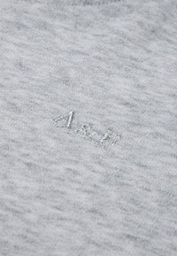 Sivá bavlnená látka s jemnou textúrou a jemným posypom. Vyšitý nápis "A&P" kovovou niťou blízko stredu.