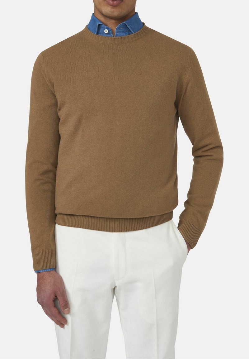 Pull en maille marron à col rond, associé à un col de chemise en denim bleu clair, porté avec un pantalon blanc, mettant en valeur un look superposé.