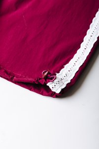 Μπορντό ύφασμα με υφή, διακοσμημένο με λευκή δαντέλα στην άκρη, στερεωμένο με διακοσμητικό κουμπί και λεπτομέρεια με πτυχώσεις υφάσματος.