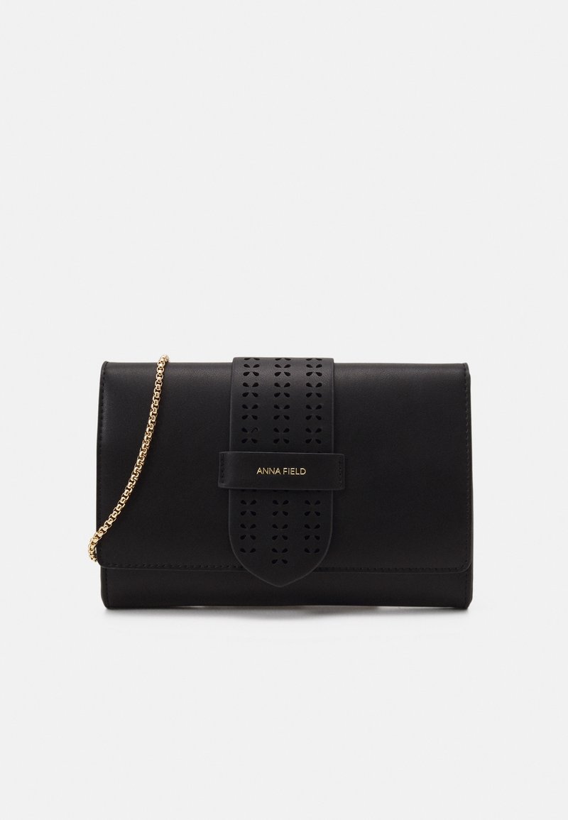 Pochette rectangulaire noire avec sangle décorative, bandoulière chaîne dorée et logo "ANNA FIELD" sur le devant.