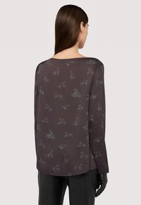 Hnědá dlouhá košile s dlouhým rukávem, s jemným vzorem siluety psa, širokým výstřihem a volným střihem. Hladká textura, minimalistický design.