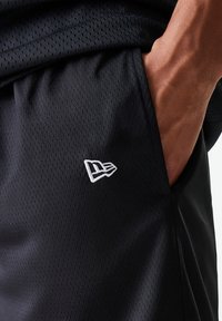 Calções de desporto pretos feitos de tecido de malha respirável. Apresentam um logo branco bordado na lateral, com uma textura suave e um cós elástico.