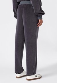 Grau Velours-Sweatpants mit entspannter Passform, elastischem Bund und Seitentaschen, kombiniert mit weißen Sneakers mit einem Logo.