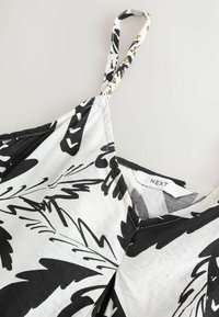 Čierno-biela látka s kvetinovým vzorom a tenkými ramienkami. Má V-výstrih a štítok s označením "NEXT". Jemná, ľahká textúra.