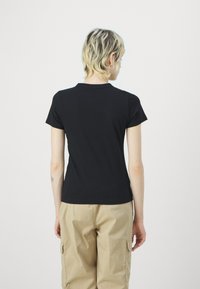 Juoda trumpa rankovė t-shirt su apvaliu iškirpimu, prigludusio silueto ir lygaus paviršiaus, derinama su kreminėmis cargo kelnėmis.
