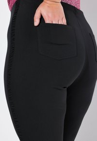 Czarne legginsy z fakturowaną, falbanistą boczną tasiemką, z tylną kieszenią i gładkim, elastycznym materiałem dla większego komfortu.