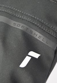 Zwarte softshell stof met een gladde textuur, voorzien van een opvallend "SOFTSHELL" label en een wit logo detail.