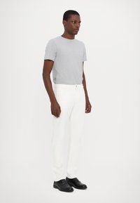 Gray short-sleeve t-shirt paired with white denim pants and black dress shoes. Model stands upright against a plain background.