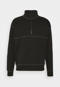 Sudadera polar negra con cuello alto, cierre de cremallera, bolsillo frontal y detalles en costuras contrastantes grises. Presenta un logotipo en el pecho.