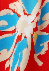 Tissu rouge présentant de grandes fleurs abstraites en bleu, crème et des touches de jaune. Texture lisse avec une palette de couleurs vibrante.