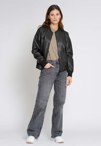 Svart läderbomberjacka med ribbade ärmslut, bärs över en beige topp. Kombineras med högmidjade grå denimjeans och vita sneakers.