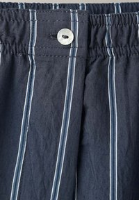 Tissu bleu foncé à rayures verticales blanches et taille élastique avec un petit bouton blanc pour la fermeture.