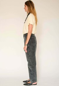 Chemise courte beige clair à manches courtes associée à un jean noir délavé taille haute. Ballerines noires avec découpes arrondies. Textures lisses, coupe décontractée.