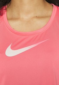 Różowa koszulka sportowa z gładkiego materiału, z okrągłym dekoltem i białym logo Nike na przodzie.