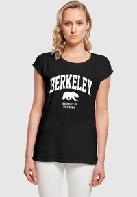 Juodas medvilninis marškinėliai su apvaliais rankovėmis, turintys baltą tekstą "BERKELEY" ir "KALIFORNIJOS UNIVERSITETAS" virš lokio grafikos.