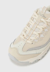 Beige athletic shoe featuring a mixed material design with leather and mesh accents, textured overlays, and a light grey outsole.